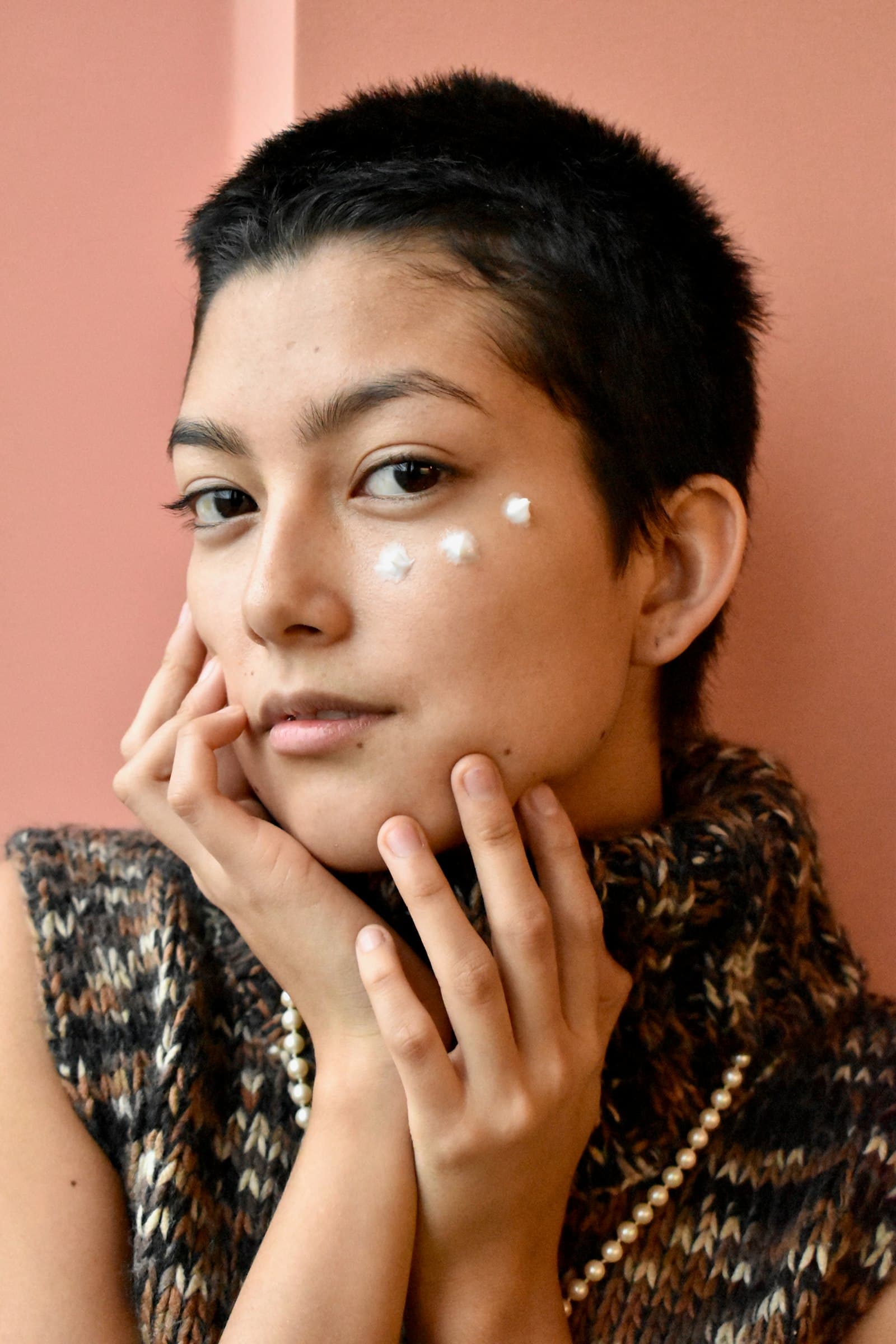 Person resting their face in their hands with three dots of white cream on one cheek