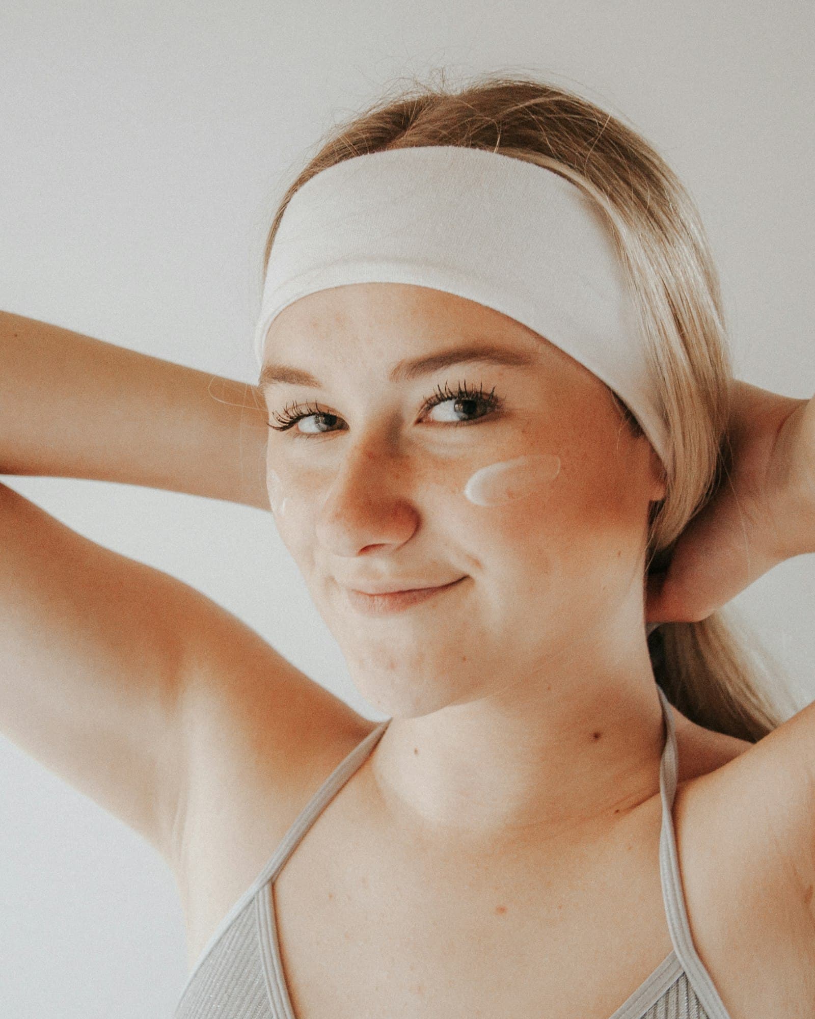 Smiling woman in a white headband with a swipe of white cream on her cheek