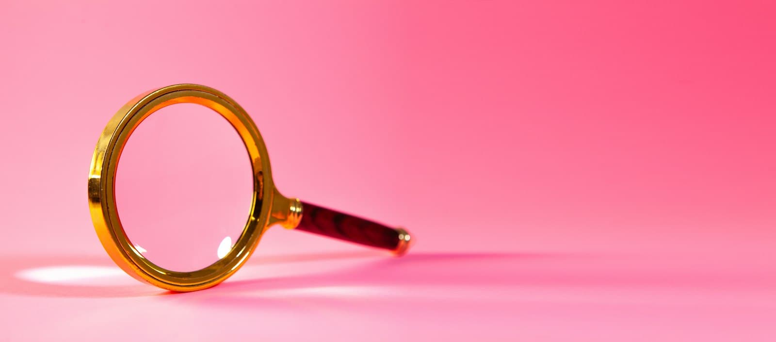 Gold magnifying glass resting on a pink background