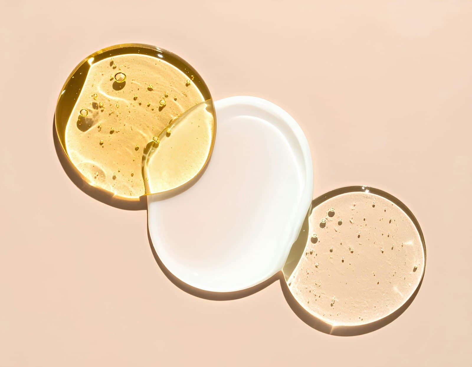 Swatches of clear gel, milky lotion and golden oil textures on a peach background