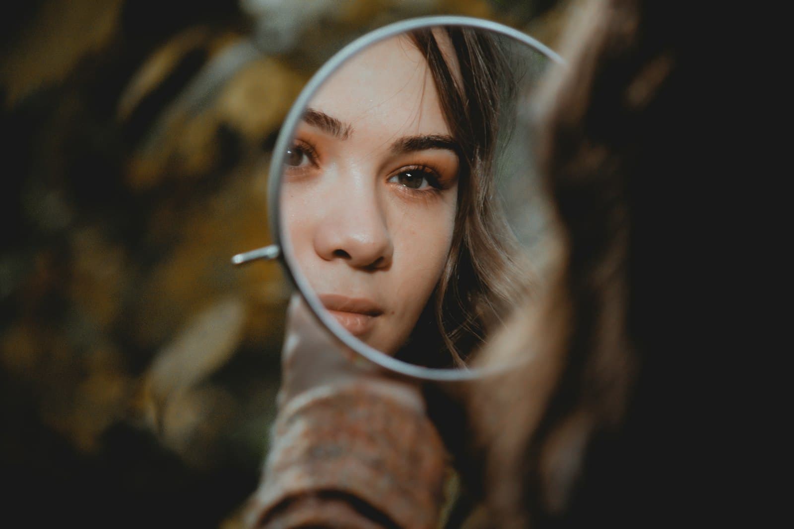 Woman checking her bare skin in a small round handheld mirror