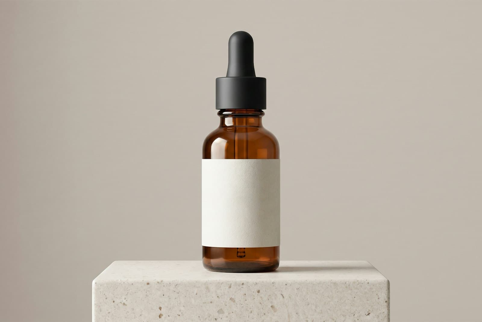 Amber glass dropper bottle with a blank label standing on a stone block against a beige wall