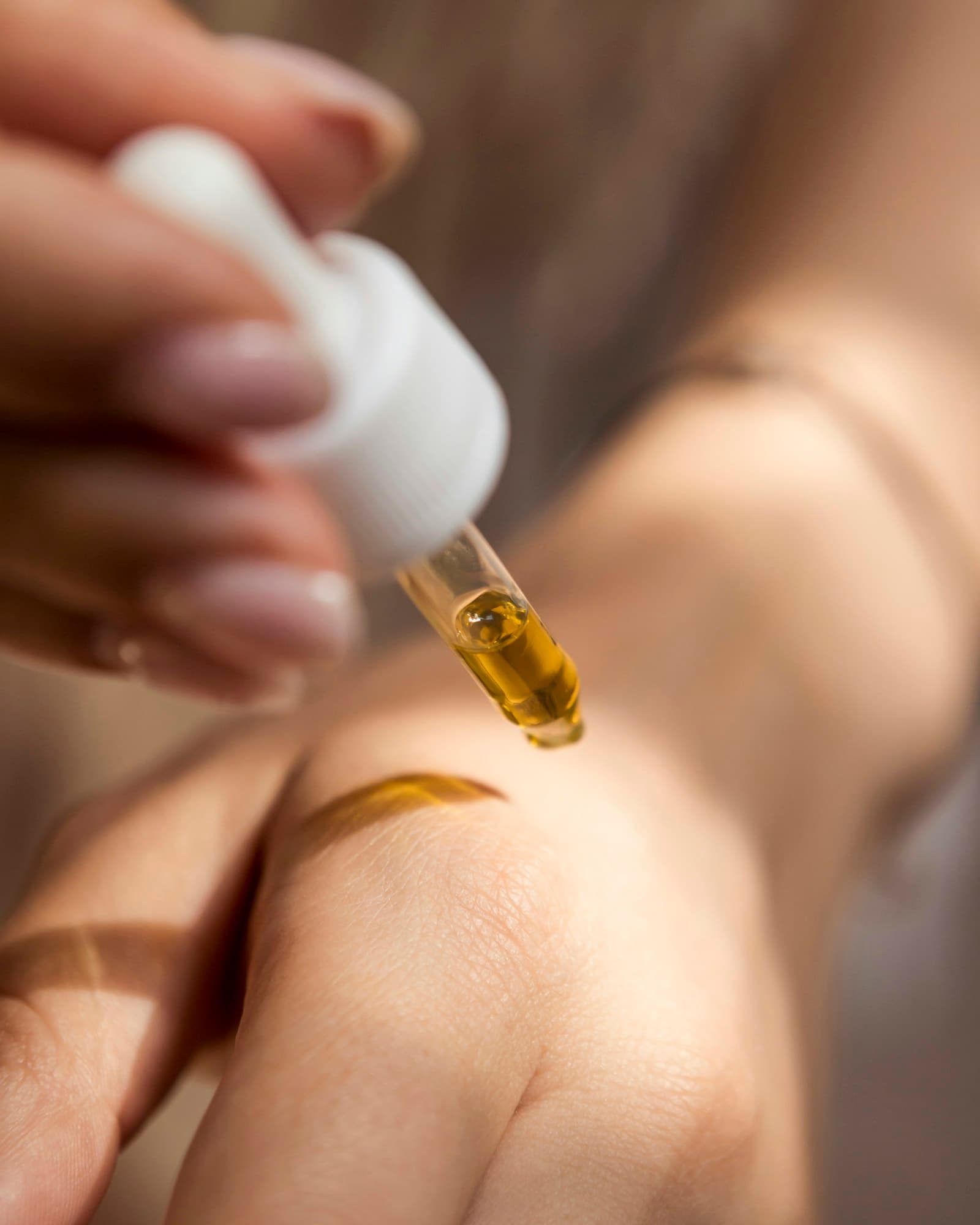 Glass dropper releasing golden serum onto the back of a hand