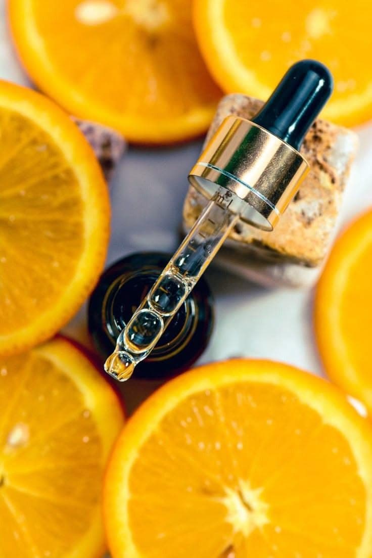 Open glass bottle of golden serum with its white dropper resting on top, beside dried grasses