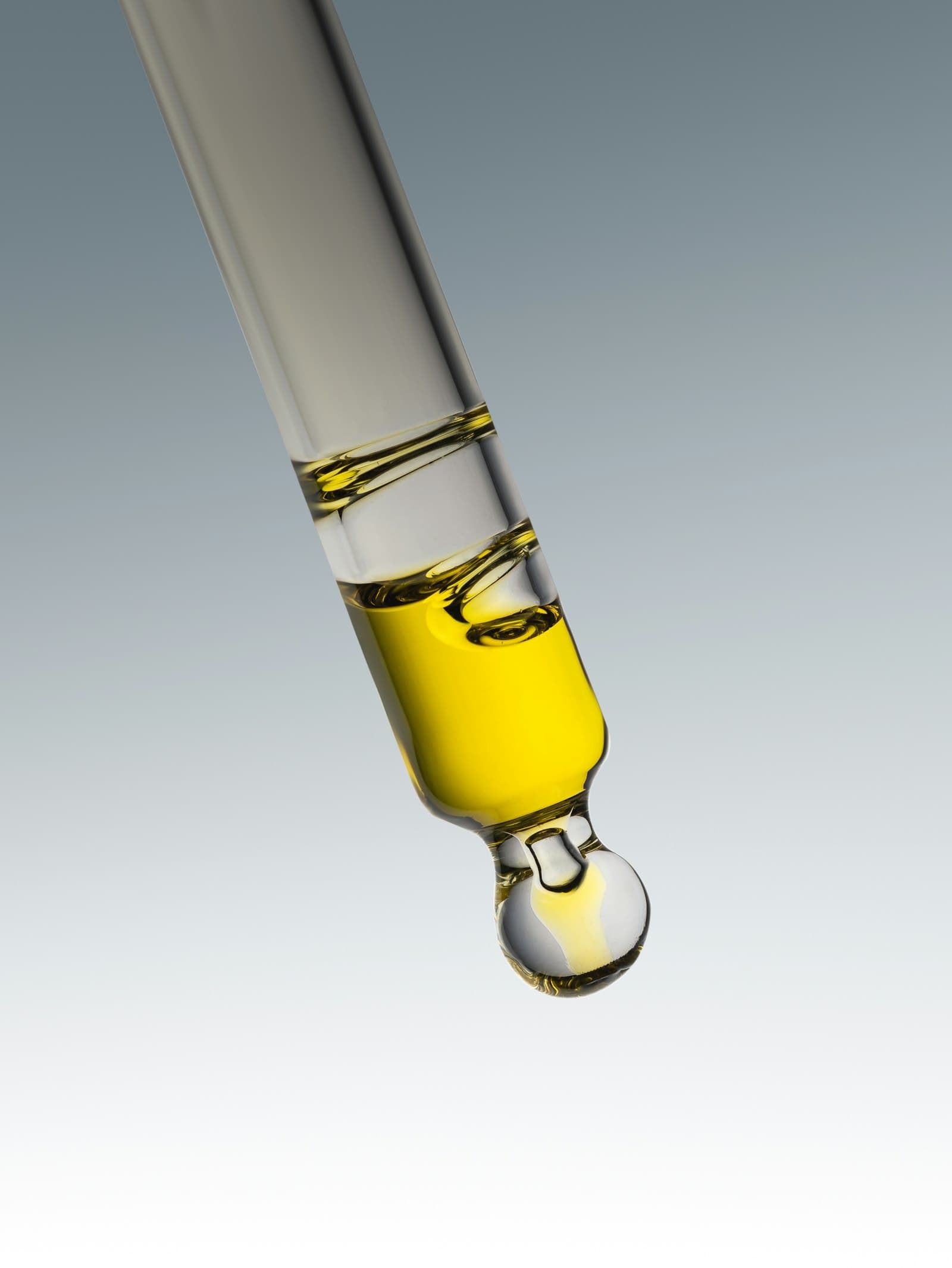 Glass pipette holding yellow serum with a drop forming at the tip