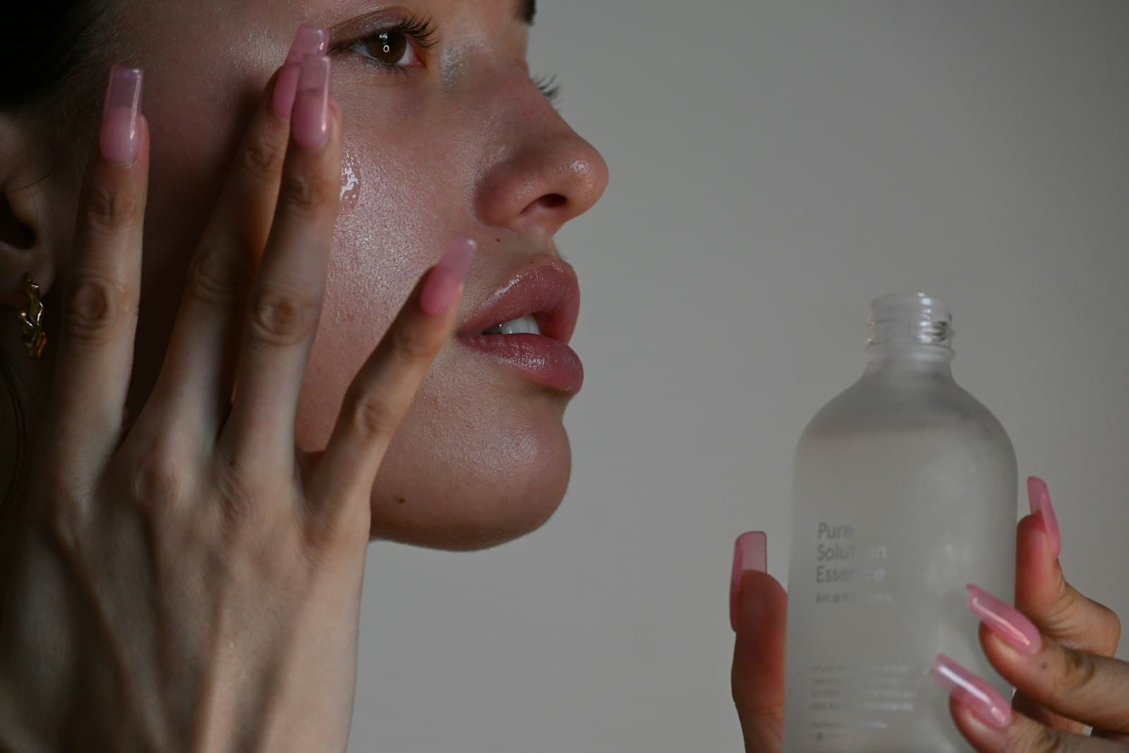 Woman with dewy skin pressing serum into her cheek while holding a frosted bottle