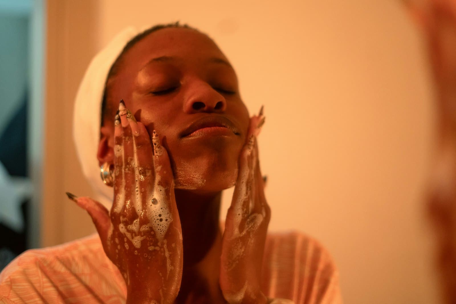 Woman massaging a lathered cleanser over her face in warm bathroom light