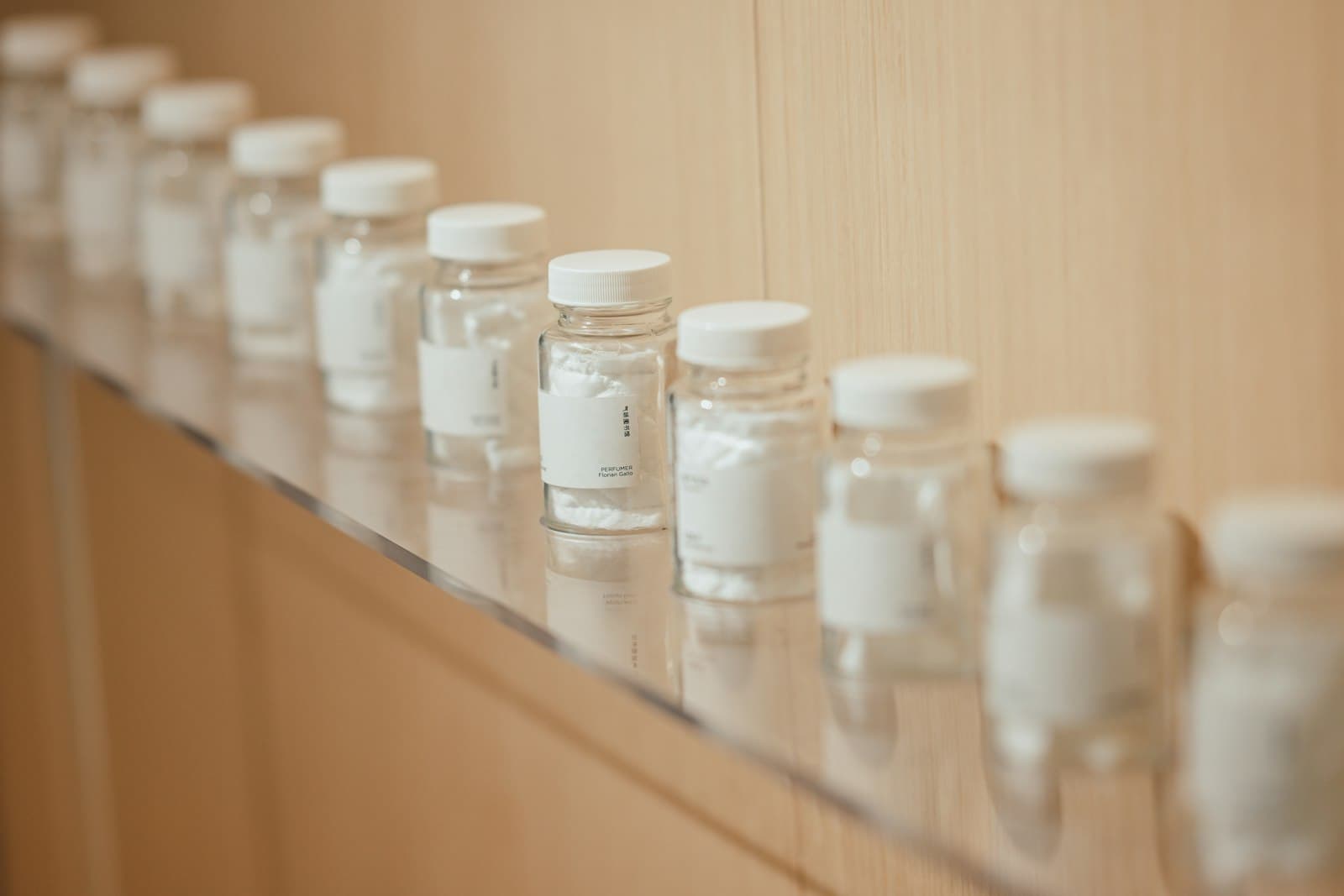 Row of small clear bottles with white caps and blank labels lined up on a shelf