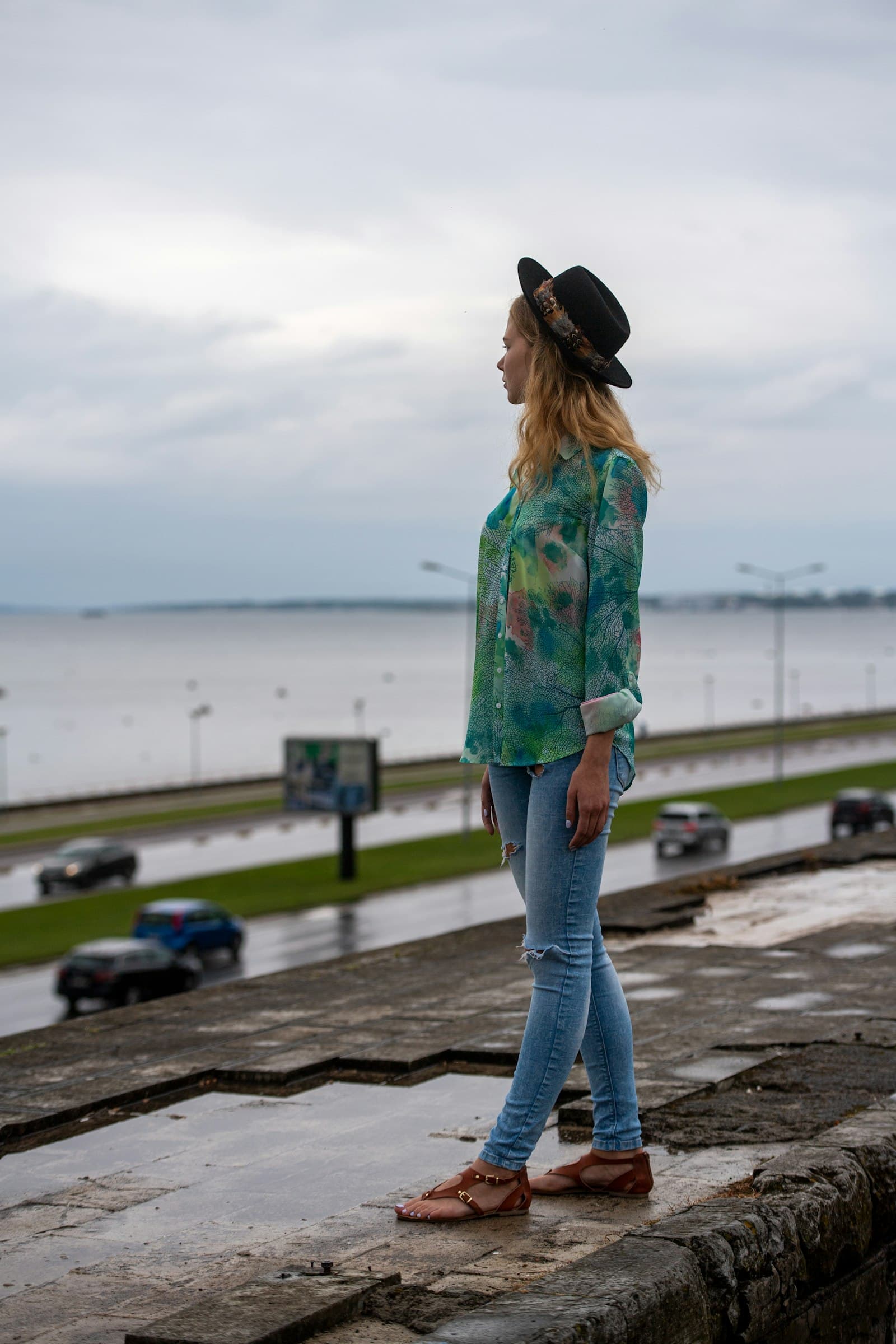 Woman in a hat standing by the water under a gray overcast sky