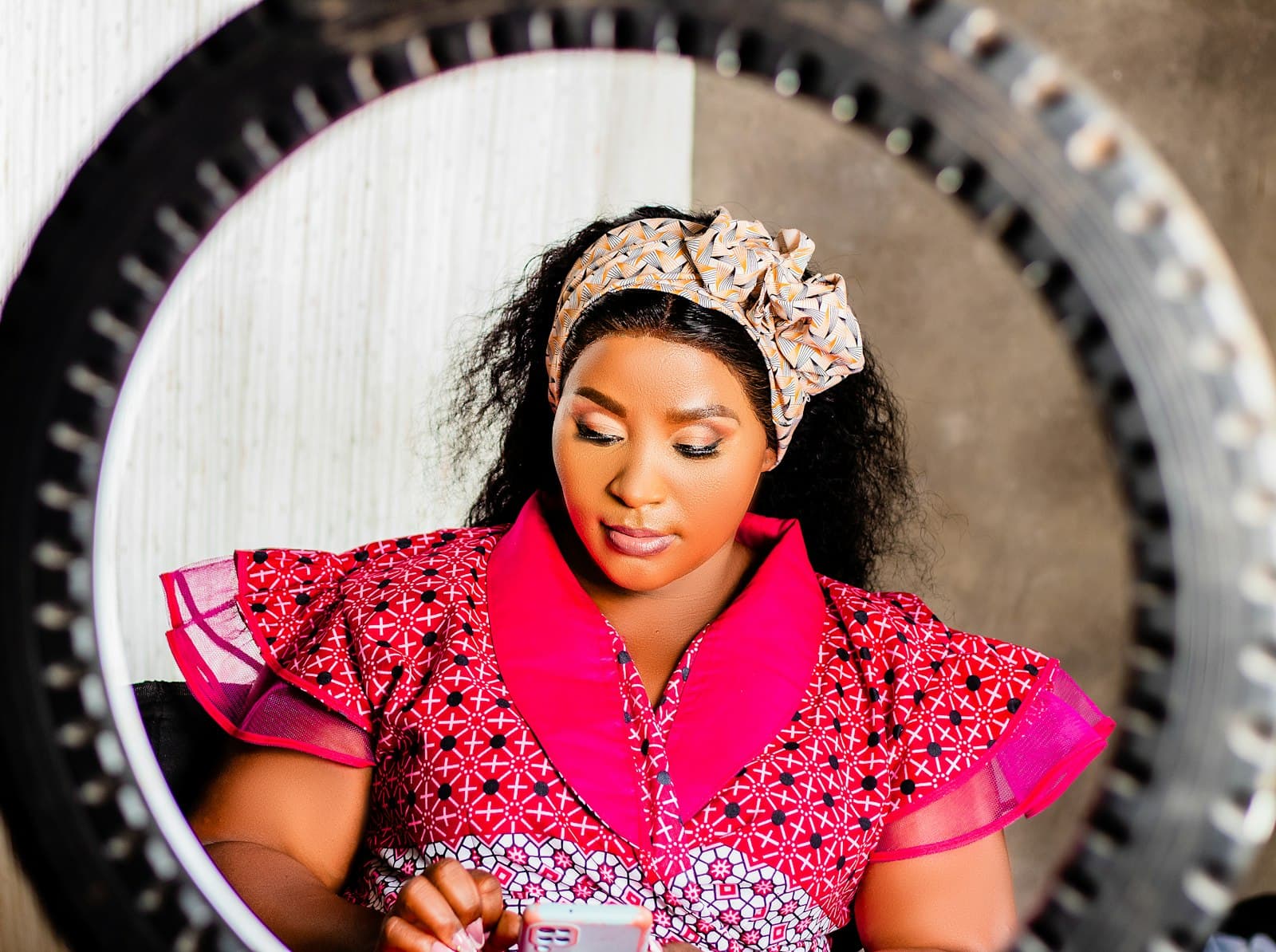 Woman in a pink patterned dress and headwrap looking down at her phone