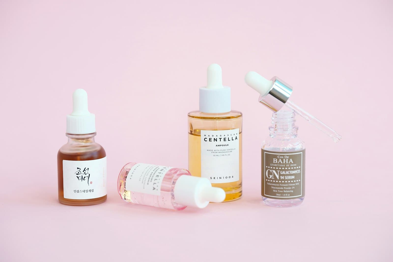 Several serum and ampoule dropper bottles arranged on a pink background
