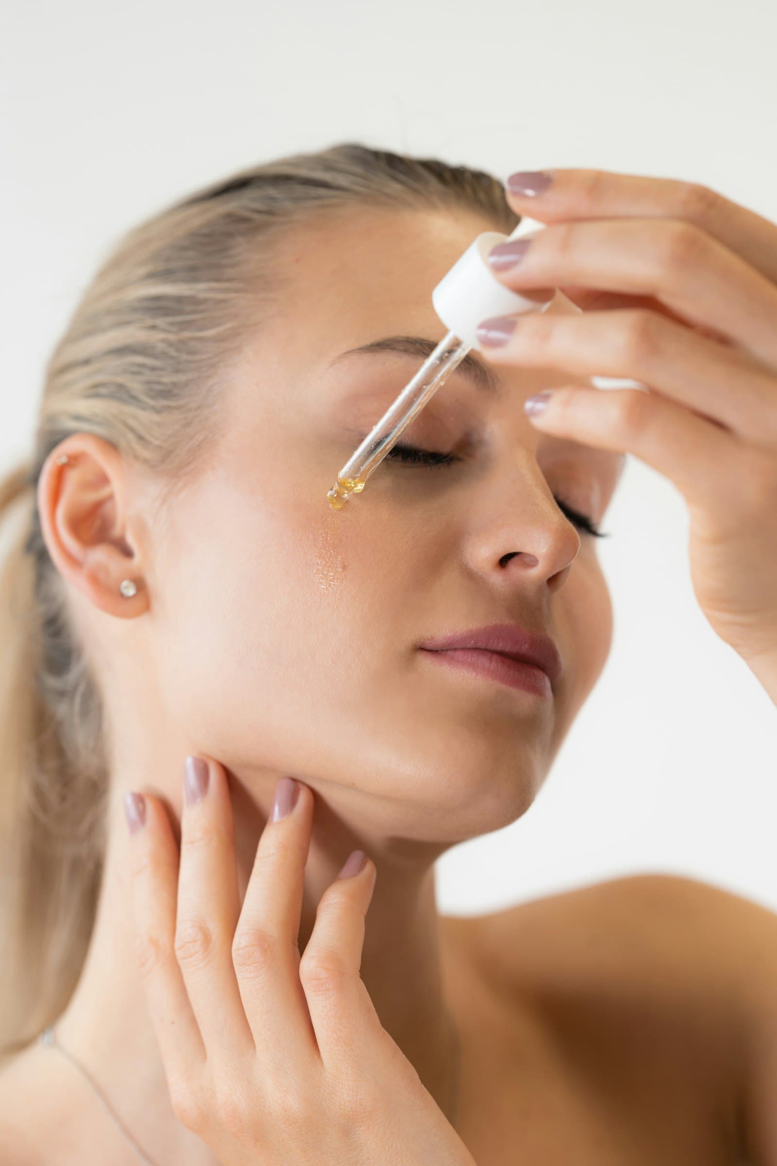 Woman applying a single drop of serum from a glass dropper near her hairline