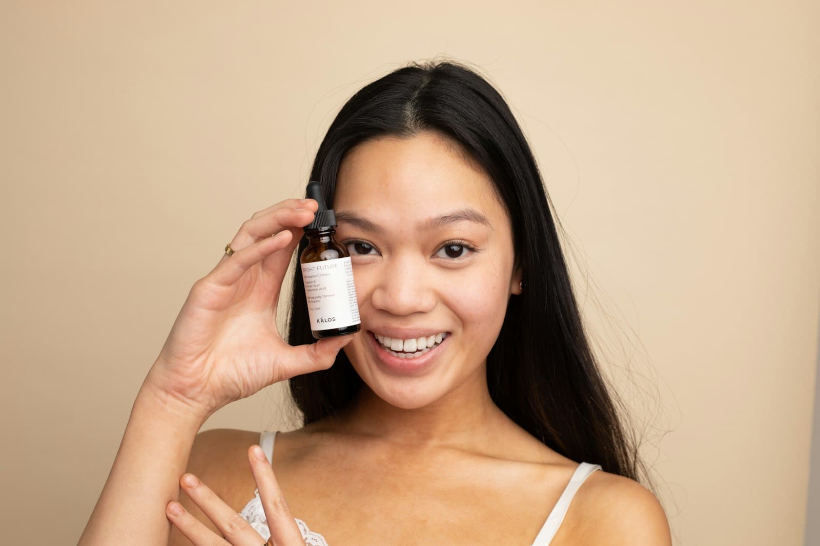 Smiling woman holding a small amber dropper bottle up beside her face