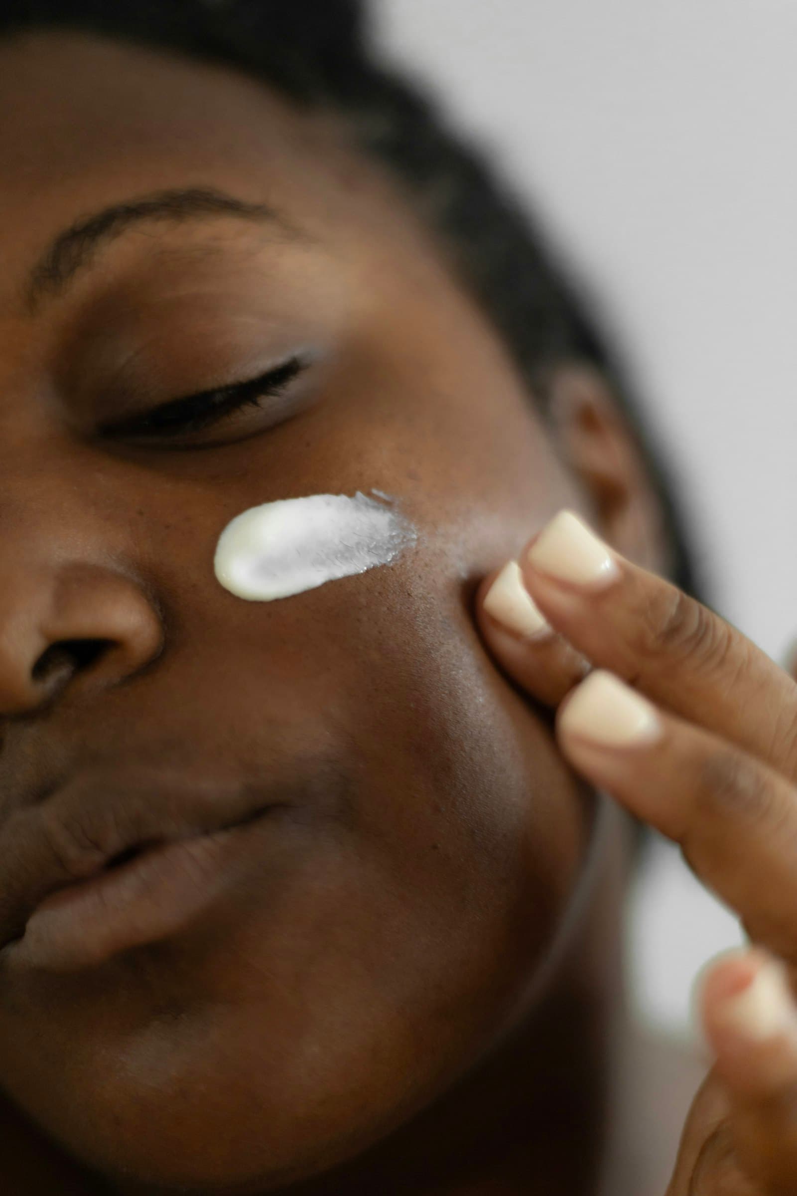 Woman dotting white cream onto her cheek with her fingertips